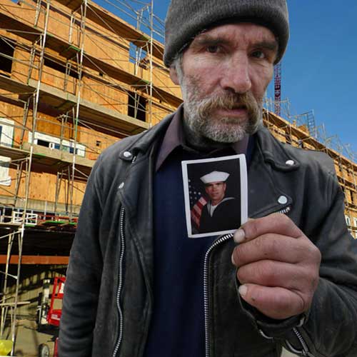 In need of housing services is a homeless Caucasian man standing in front of apartment building under constructions. He is holding a picture of himself in Navy uniform.